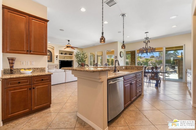 kitchen with light tile patterned floors, stainless steel dishwasher, sink, decorative light fixtures, and a center island with sink