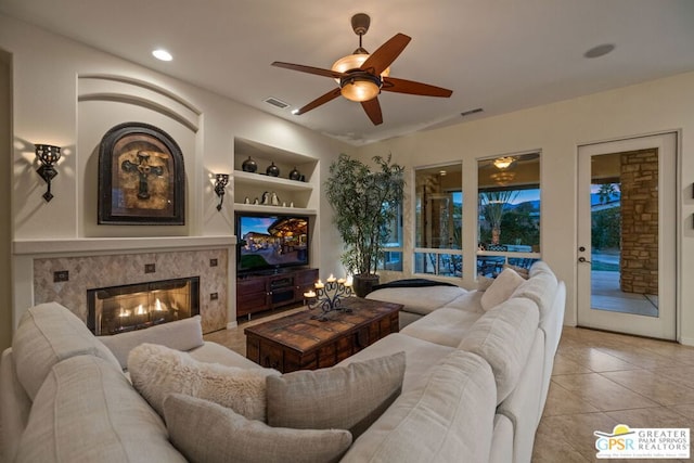 living room featuring built in shelves, ceiling fan, a tile fireplace, and light tile patterned floors