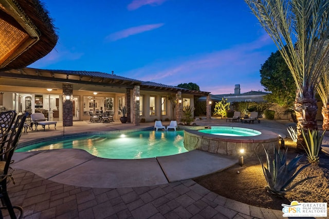 pool at dusk featuring an in ground hot tub and a patio