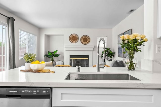 kitchen with dishwasher, sink, white cabinetry, light stone counters, and a fireplace