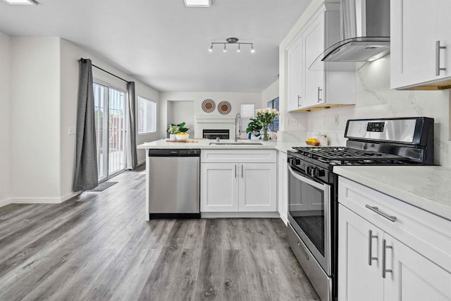 kitchen with kitchen peninsula, white cabinetry, wall chimney range hood, and appliances with stainless steel finishes