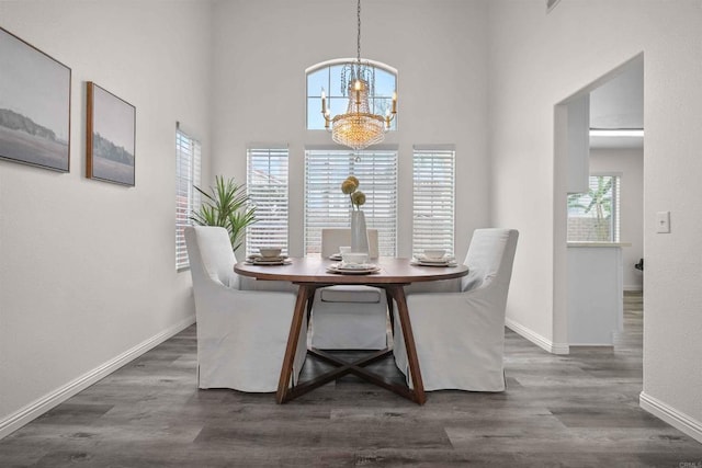 dining room with plenty of natural light, dark hardwood / wood-style floors, a towering ceiling, and a notable chandelier