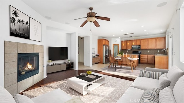 living room featuring ceiling fan, sink, a tile fireplace, and light wood-type flooring