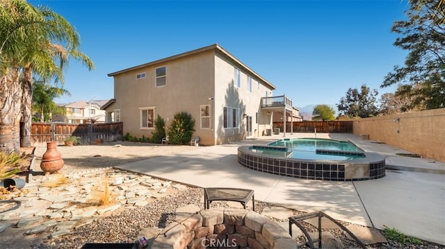 back of property featuring an in ground hot tub, a balcony, and a patio area