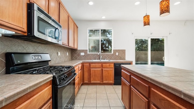 kitchen with black appliances, tile counters, sink, hanging light fixtures, and light tile patterned floors