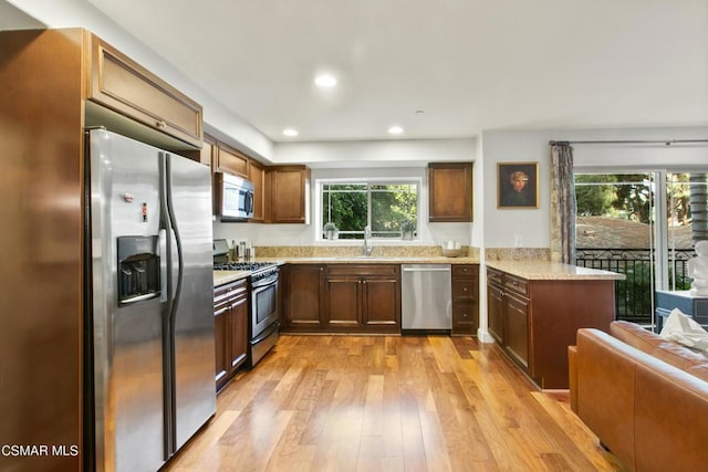 kitchen featuring light hardwood / wood-style floors, sink, kitchen peninsula, stainless steel appliances, and light stone counters