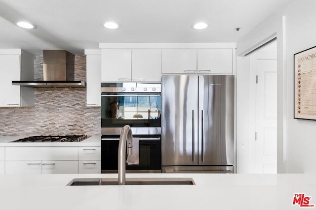 kitchen featuring decorative backsplash, white cabinetry, stainless steel appliances, and wall chimney exhaust hood