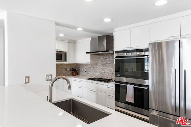 kitchen featuring wall chimney exhaust hood, sink, white cabinets, decorative backsplash, and stainless steel appliances