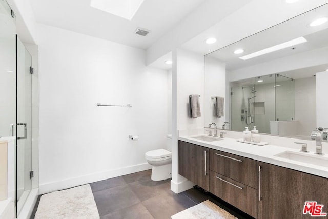 bathroom featuring toilet, a shower with shower door, a skylight, and vanity