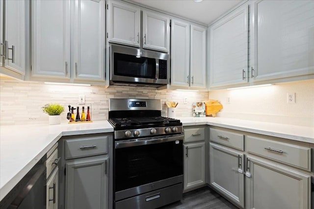 kitchen with gray cabinets, dark wood-type flooring, decorative backsplash, and stainless steel appliances