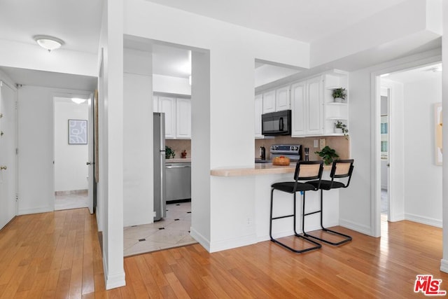 kitchen featuring kitchen peninsula, backsplash, white cabinetry, a kitchen bar, and stainless steel appliances