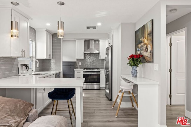 kitchen with pendant lighting, white cabinetry, wall chimney range hood, stainless steel appliances, and a kitchen breakfast bar