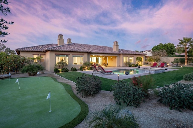 back house at dusk featuring a fenced in pool and a patio