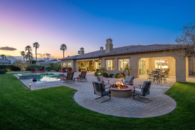 back house at dusk featuring an outdoor fire pit, a patio, and a lawn