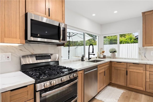 kitchen with sink, light stone counters, light hardwood / wood-style floors, and appliances with stainless steel finishes