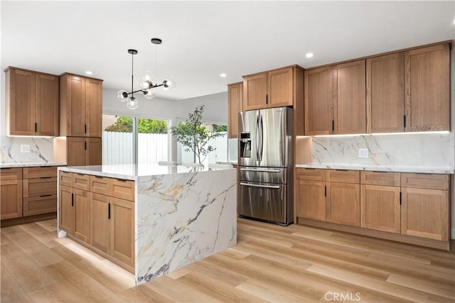 kitchen featuring a center island, decorative light fixtures, backsplash, stainless steel fridge with ice dispenser, and light wood-type flooring