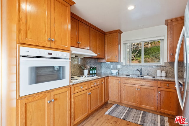 kitchen with sink, light wood-type flooring, tasteful backsplash, light stone counters, and white appliances