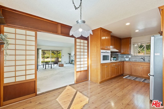 kitchen with stainless steel refrigerator, light wood-type flooring, decorative light fixtures, white oven, and backsplash