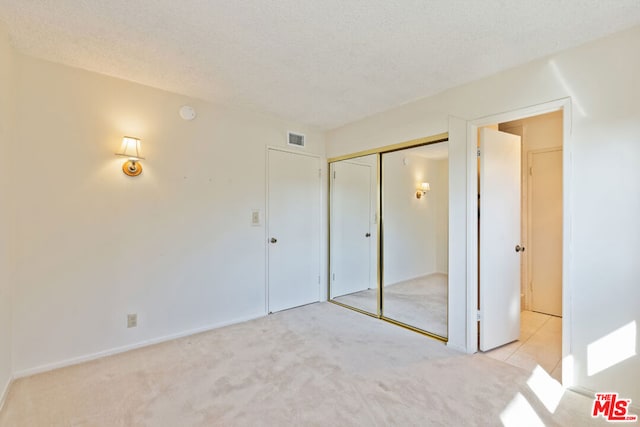 unfurnished bedroom with a closet, light colored carpet, and a textured ceiling