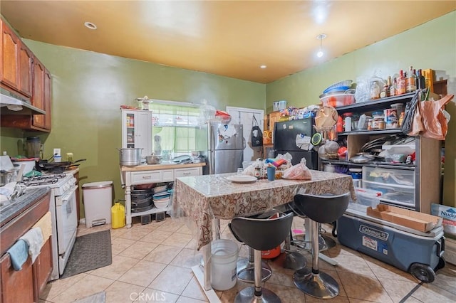 kitchen featuring freestanding refrigerator, light tile patterned floors, and white gas range