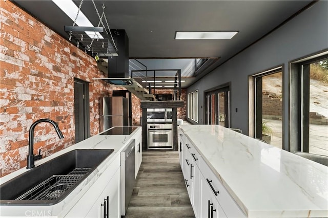 kitchen featuring light stone countertops, appliances with stainless steel finishes, a kitchen island, white cabinetry, and sink