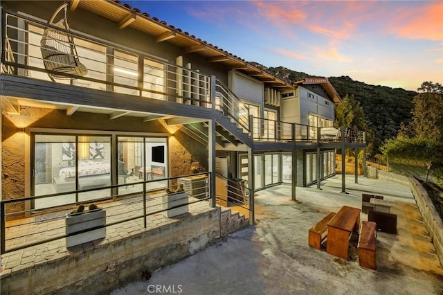 back house at dusk with a balcony and a patio area