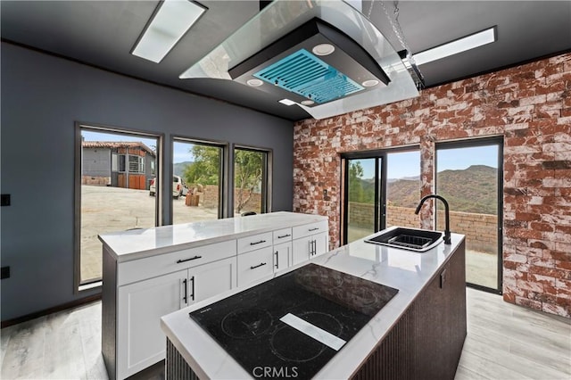 kitchen featuring brick wall, white cabinets, sink, a center island with sink, and black electric cooktop