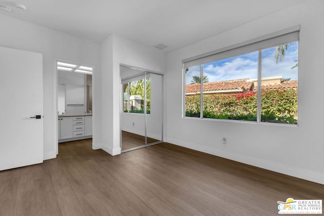 unfurnished bedroom featuring hardwood / wood-style floors, a closet, and ensuite bathroom