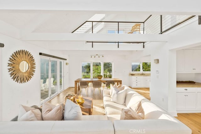 living room featuring beamed ceiling, a skylight, sink, and light wood-type flooring