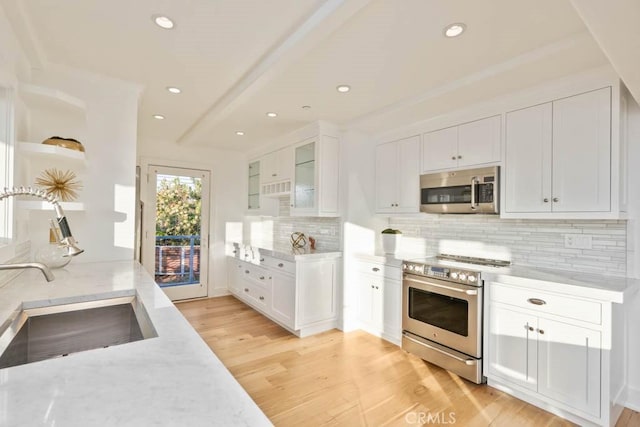 kitchen with sink, white cabinetry, light stone counters, light wood-type flooring, and appliances with stainless steel finishes