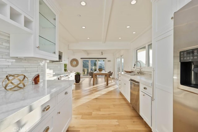 kitchen with sink, stainless steel appliances, beam ceiling, light stone countertops, and white cabinets