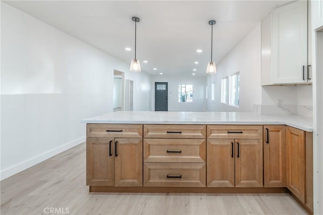 kitchen featuring light wood-type flooring, decorative light fixtures, kitchen peninsula, and light stone countertops