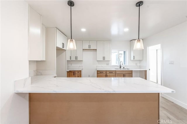 kitchen featuring light stone countertops, pendant lighting, white cabinets, sink, and kitchen peninsula