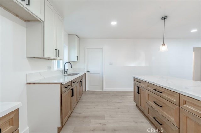 kitchen featuring sink, decorative light fixtures, white cabinetry, and light hardwood / wood-style flooring