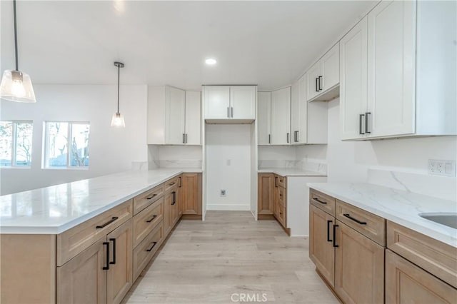 kitchen with light hardwood / wood-style floors, light stone countertops, white cabinets, kitchen peninsula, and pendant lighting