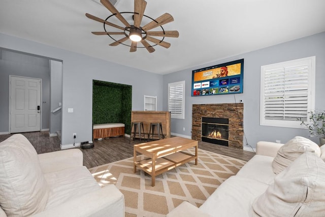 living room with hardwood / wood-style flooring, ceiling fan, and a stone fireplace