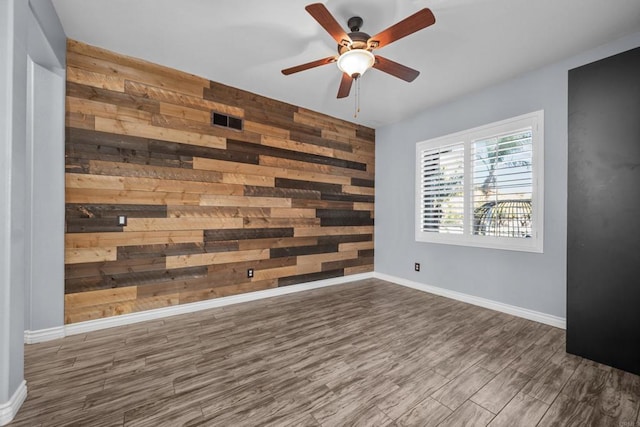 empty room featuring wood walls, ceiling fan, and dark hardwood / wood-style flooring