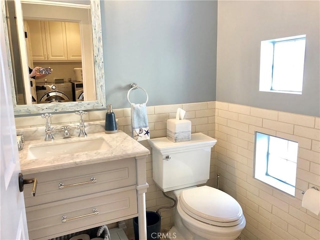 bathroom featuring separate washer and dryer, toilet, vanity, and tile walls