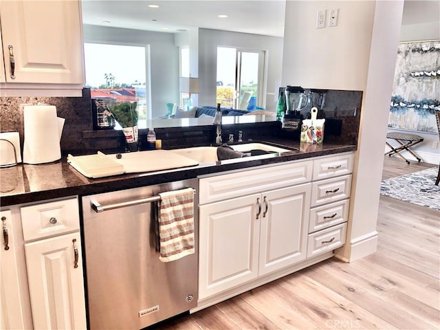 kitchen with stainless steel dishwasher, white cabinets, sink, light hardwood / wood-style flooring, and backsplash