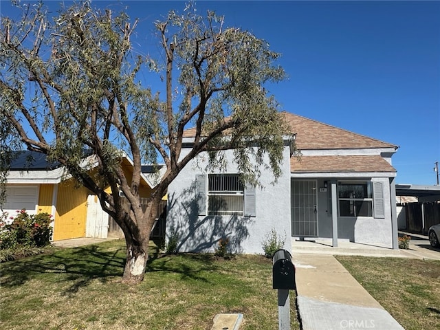 view of front of property with stucco siding, a front yard, and roof with shingles