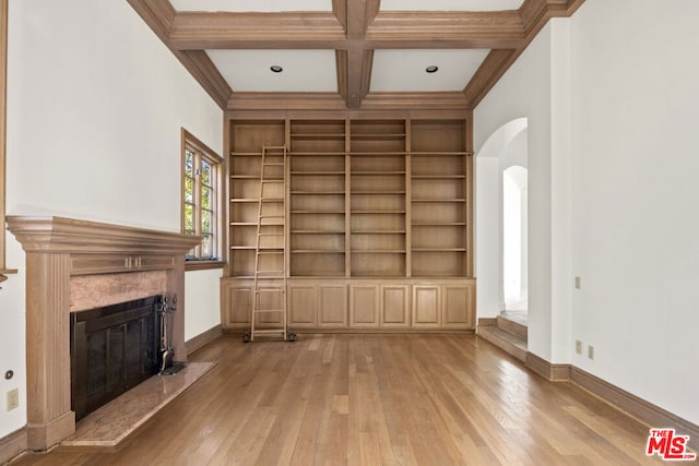 unfurnished living room with built in shelves, coffered ceiling, beamed ceiling, a premium fireplace, and light hardwood / wood-style floors