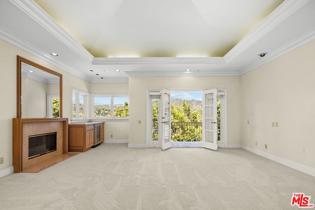 unfurnished living room featuring a healthy amount of sunlight, light colored carpet, ornamental molding, and a tray ceiling