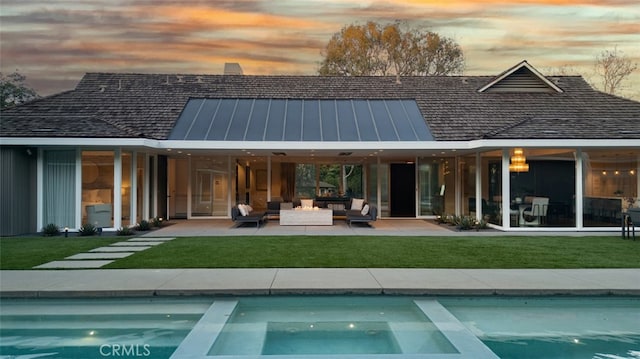 back house at dusk with outdoor lounge area, a lawn, and a patio