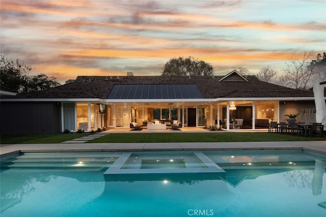 back house at dusk featuring an outdoor living space, a patio, a lawn, and solar panels