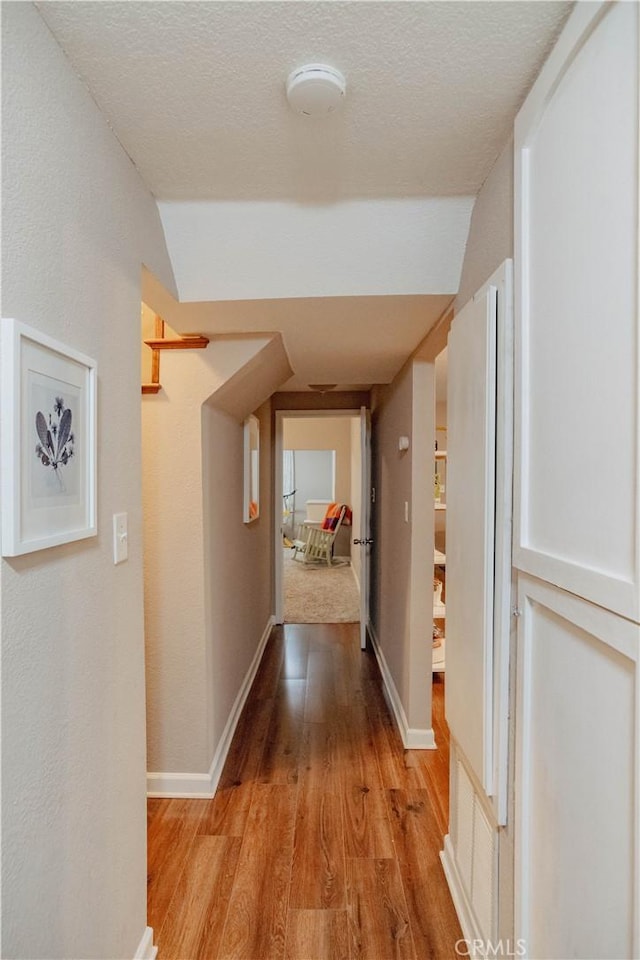 hallway featuring baseboards, a textured ceiling, and light wood-style flooring