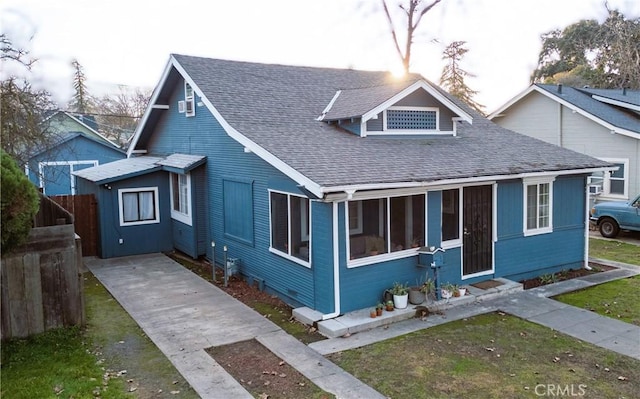 bungalow featuring a front lawn, roof with shingles, fence, and driveway