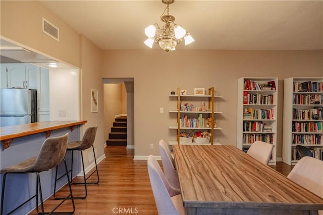 dining area with an inviting chandelier, visible vents, baseboards, light wood-style floors, and stairs