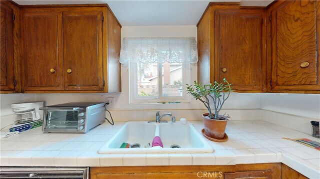 kitchen with tile countertops, dishwashing machine, and sink