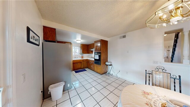 kitchen featuring light tile patterned floors, stainless steel fridge, black double oven, and a textured ceiling