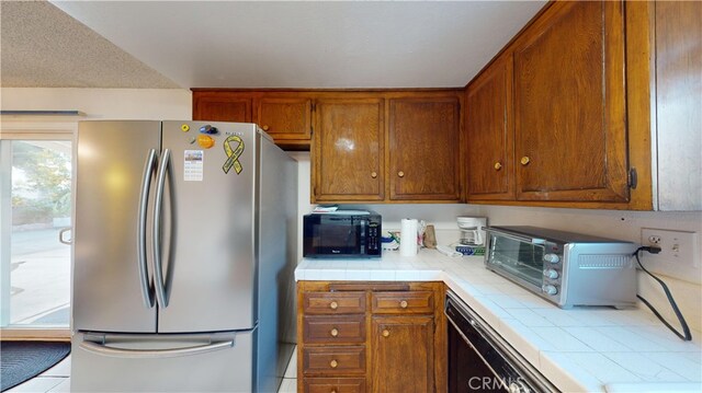 kitchen with light tile patterned flooring, tile countertops, and stainless steel refrigerator